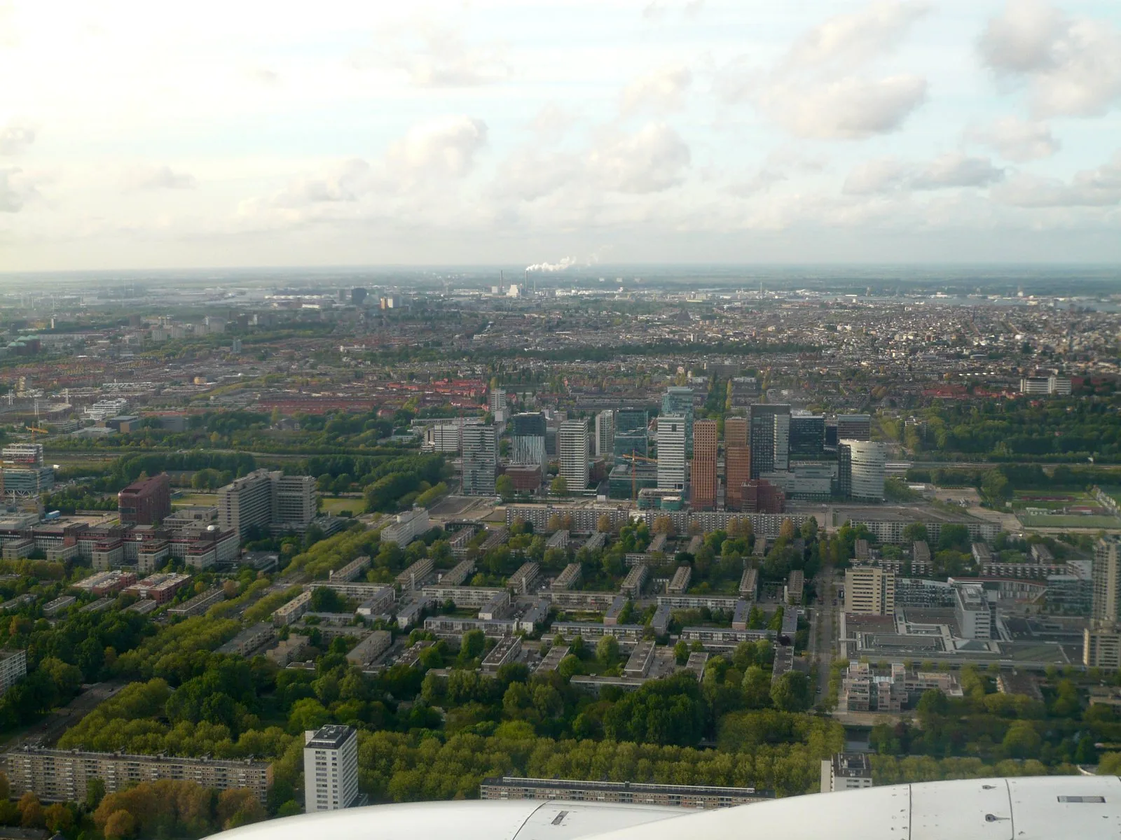Overhead aerial of Amsterdam's Zuidas business district straddling the A10 South ring road and rail corridor, showing the transit-oriented corridor layout of the Zuidas plan. The actual Zuidas Develop