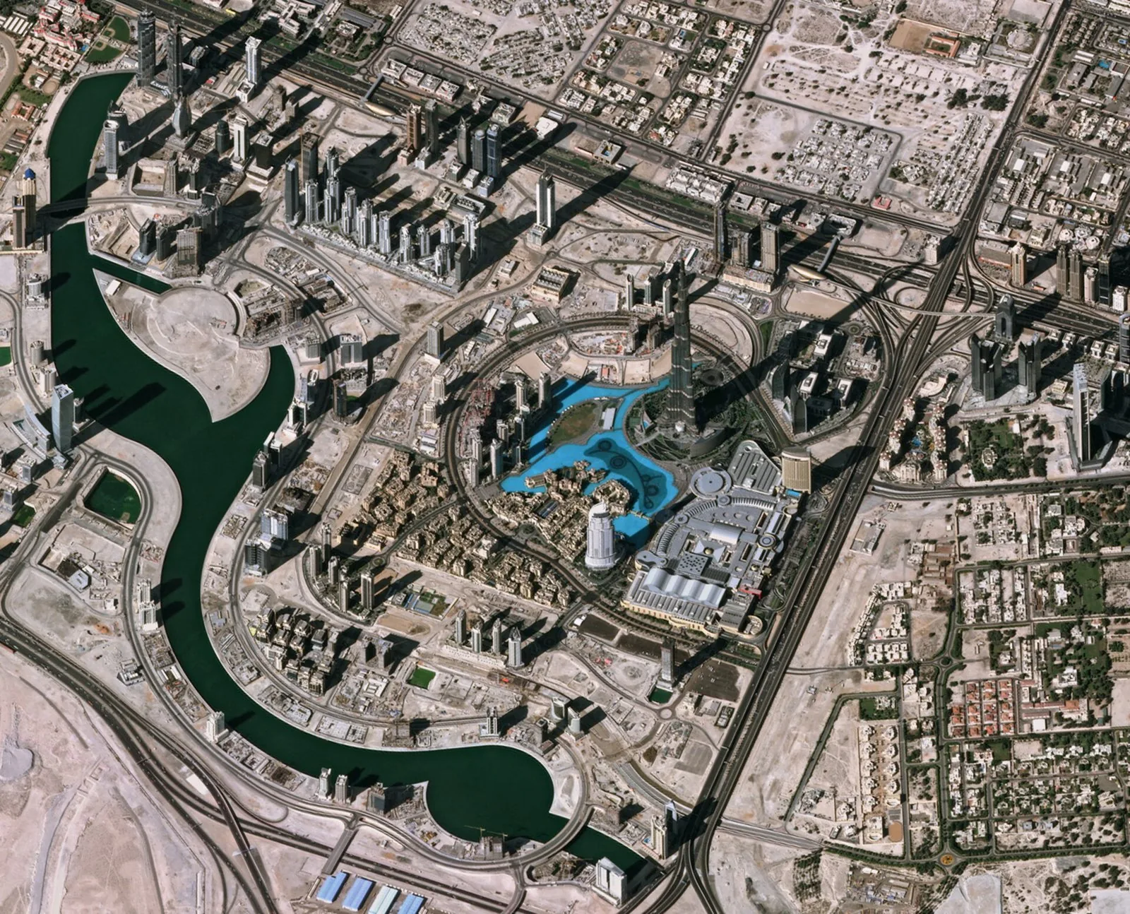 Top-down Pléiades satellite image of Downtown Dubai in which the Emaar masterplan geometry is legible: Burj Khalifa and its shadow, the Burj Khalifa Lake / Dubai Fountain, The Dubai Mall, and the surr